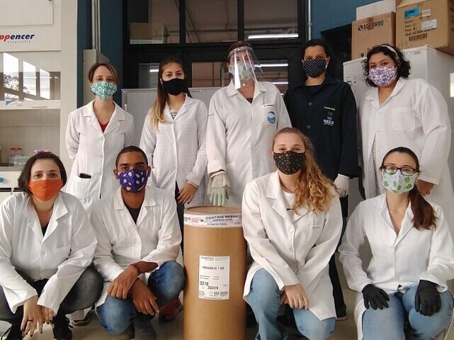 chemists posing with masks in front of a barrel
