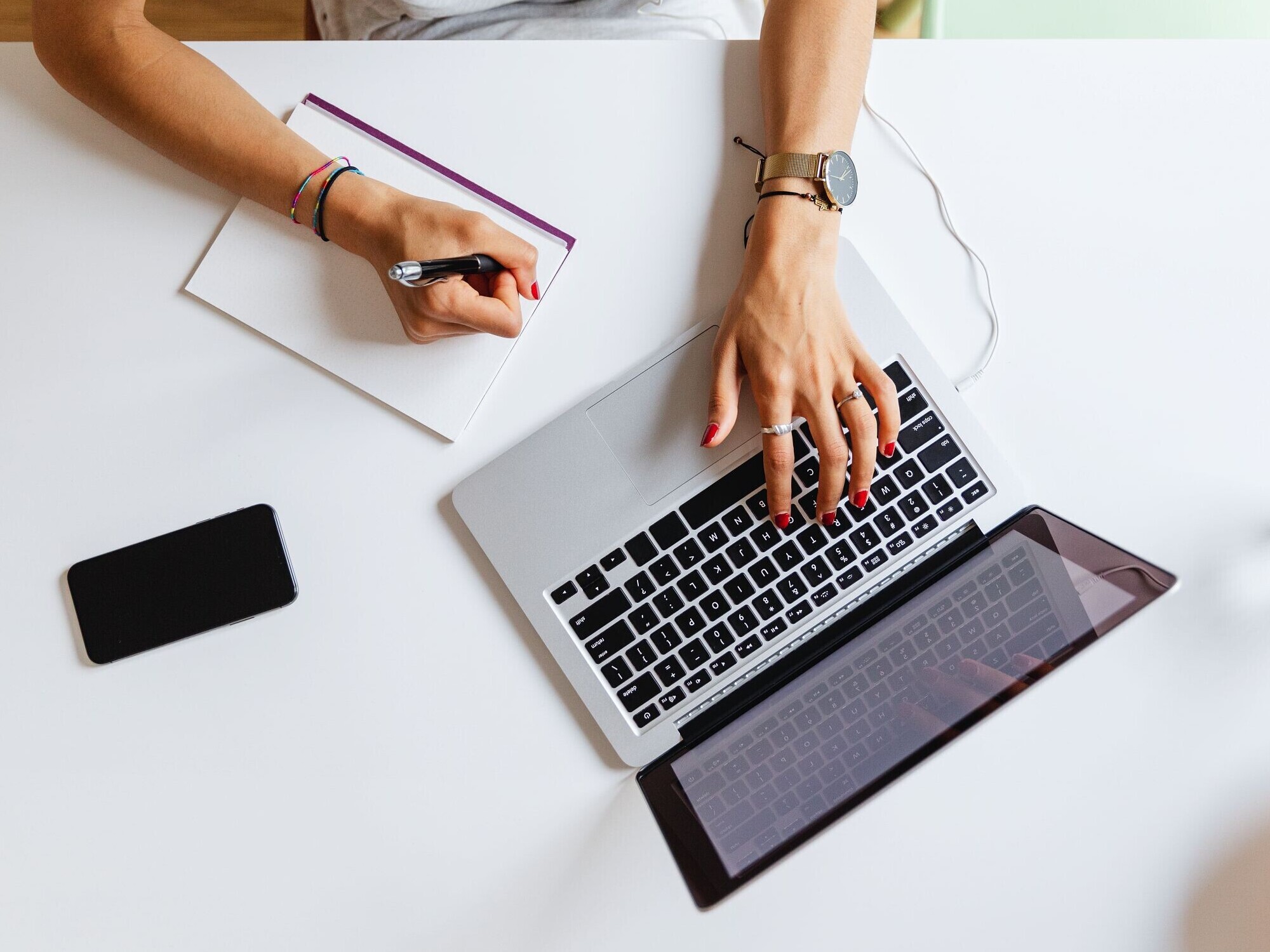 Laptop on a white desk, woman's arms on it.